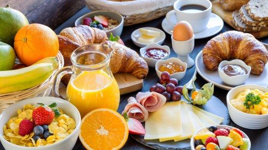 ontbijttafel met fruitsap, brood, koeken, ontbijtgranen, verschillende soorten fruit en beleg, koffie ...